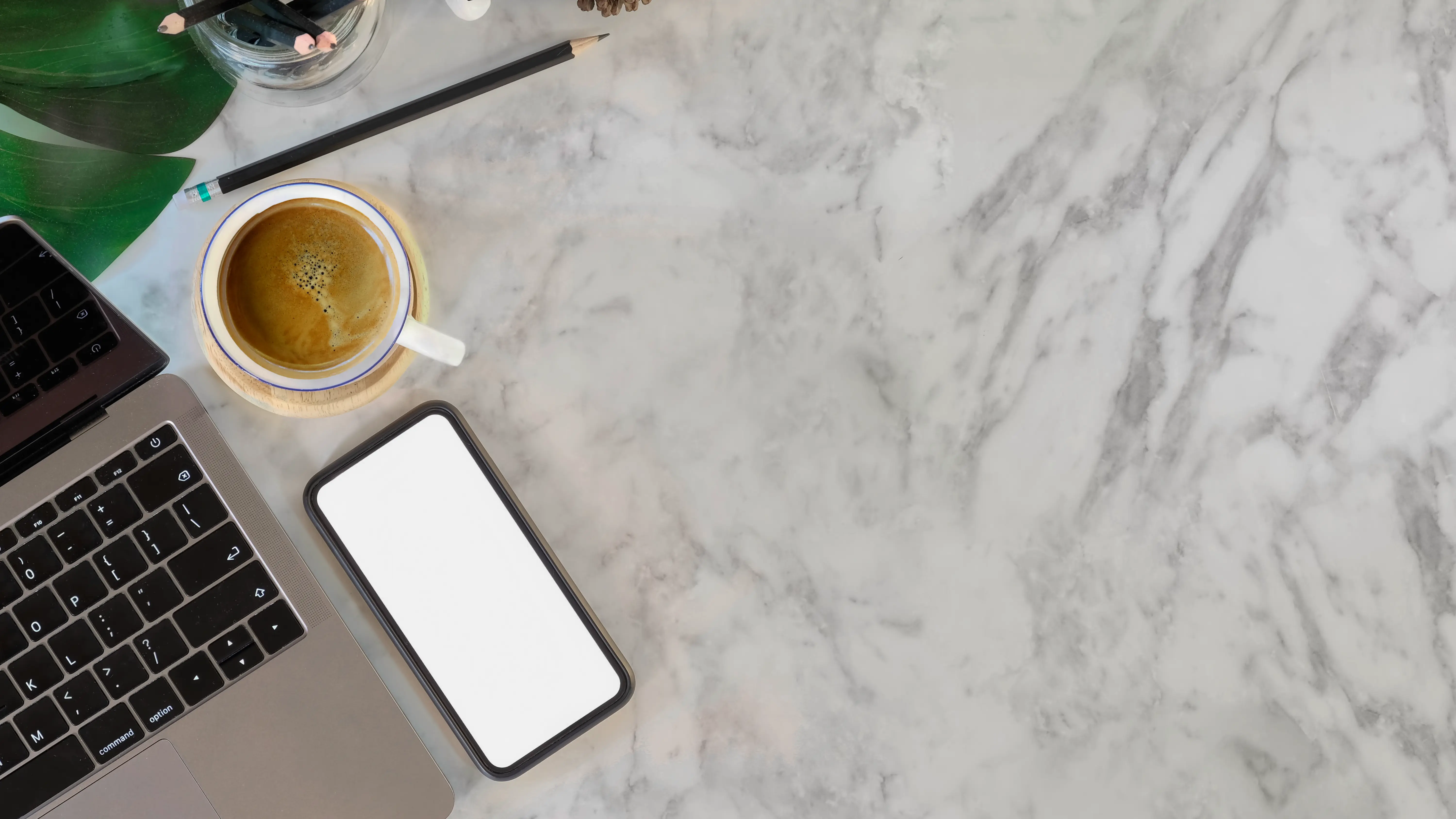 A table of granite on which there are a phone, cup of coffee and a laptop place on the left side